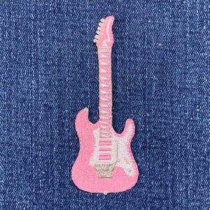 May include: Pink embroidered electric guitar patch. The patch is on a blue denim background.