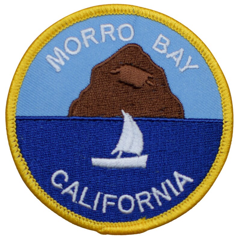 May include: A blue and yellow embroidered patch with the words "MORRO BAY CALIFORNIA" and a brown rock formation with a sailboat in front of it.
