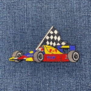 May include: Embroidered patch of a Formula 1 race car with a checkered flag. The car is yellow, red, and blue, with the text "F-1" and "TOP". The patch is on a blue denim background.