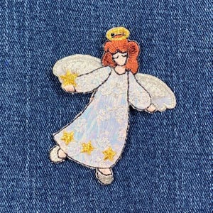 May include: Embroidered iron-on patch of an angel with a halo, white dress, and gold stars. The angel has red hair and is holding a gold star.
