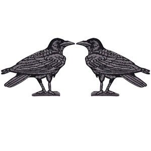 May include: Two embroidered patches featuring detailed depictions of crows in profile. The crows are in a dark gray color, with intricate feather and wing details. The patches are designed to be ironed or sewn onto fabric.