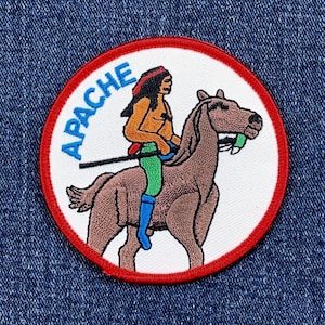 May include: Embroidered patch featuring an Apache warrior riding a brown horse. The patch has a white background with a red border and the word "APACHE" in blue. The warrior is depicted with a red headband, green pants, and blue boots.