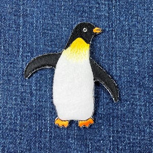 Könnte beinhalten: Gestickter Pinguin-Aufnäher mit weißem Körper, schwarzen Flügeln und Kopf sowie gelben und orangefarbenen Akzenten. Der Aufnäher ist zum Aufnähen oder Aufbügeln auf Stoff geeignet.