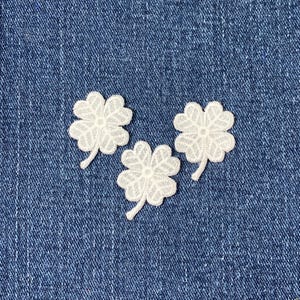 May include: Three white four-leaf clover patches on a blue denim background.