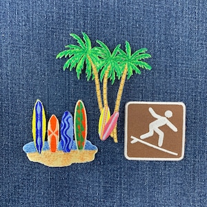 May include: Three embroidered patches featuring a tropical scene with three green palm trees, a group of four colorful surfboards standing on a sandy beach, and a square brown patch with a white graphic of a person surfing on a surfboard.