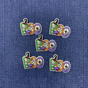 May include: Five embroidered patches featuring the word BOO in green, orange, and purple thread. Each letter B is topped with a black witch hat, the letter O contains a spider web design, and a small purple spider is attached to the bottom.