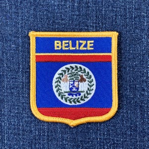 May include: Embroidered patch featuring the flag of Belize. The patch has a blue background with the word "BELIZE" in gold. A red stripe separates the top and bottom blue sections. The center features a circular emblem with a detailed design.