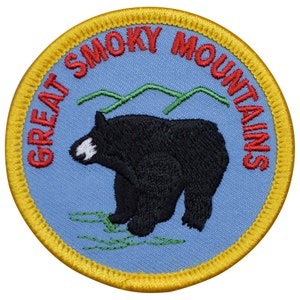May include: A blue and yellow embroidered patch with the text "Great Smoky Mountains" in red lettering. A black bear is standing on a green patch of grass.