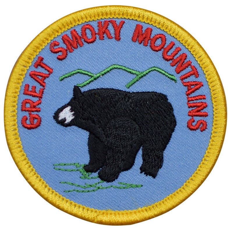 May include: A blue and yellow embroidered patch with the text "Great Smoky Mountains" in red lettering. A black bear is standing on a green patch of grass.