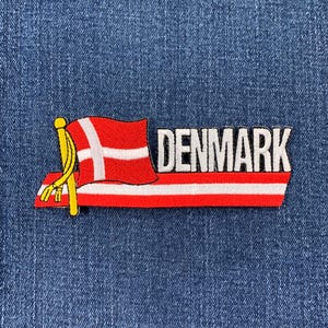 May include: Red, white, and yellow embroidered patch with the Danish flag and the word "DENMARK" on a blue denim background.
