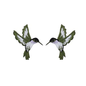 May include: Two embroidered hummingbird patches featuring olive green wings with white accents, a black head, and a white chest. The birds are depicted in a flying position with wings extended, showcasing detailed thread work and a clean, stitched edge.