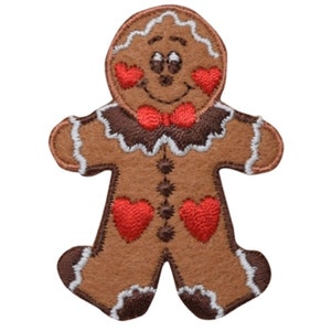 Könnte beinhalten: Ein brauner Lebkuchenmann-Aufnäher mit einem lächelnden Gesicht, roten Herzbacken und einer roten Fliege. Der Aufnäher hat weiße Zuckergussdetails und ist eine festliche Weihnachtsdekoration.