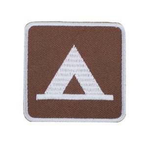 May include: A square-shaped embroidered patch featuring a brown background with a white border. Centered on the patch is a white graphic icon of a tent, depicted as a triangle with a horizontal base line, creating a clear, high-contrast design.