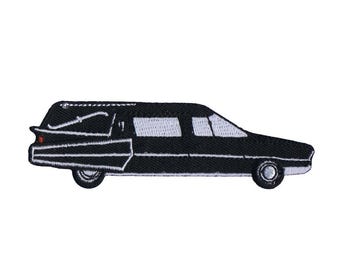May include: An embroidered patch shaped like a black hearse with white window detailing, a white trim line along the body, and a small red accent on the rear tail light. The vehicle is depicted in a side profile view with two black wheels.
