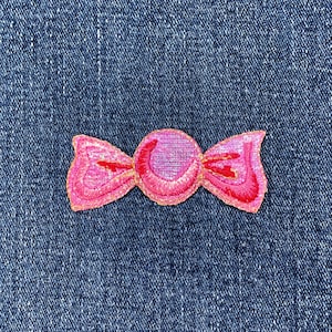 May include: Embroidered candy-shaped patch. The patch has a pink centre with pink and red detailing, and a gold outline. It is set against a blue denim background.