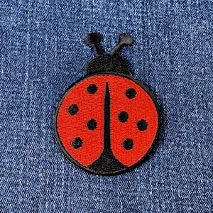 May include: An embroidered ladybird patch in red and black, featuring black spots and antennae. The patch has a black border and is set against a blue denim background.