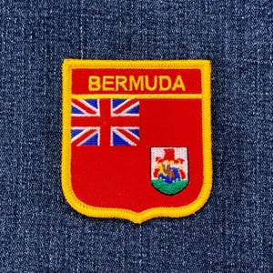 May include: A Bermuda flag patch with a red background and a yellow border. The patch features the Union Jack in the upper left corner and a coat of arms in the lower right corner. The word "BERMUDA" is at the top.