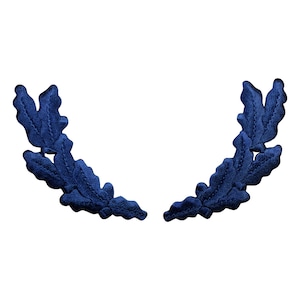 Pu&ograve; includere: Un paio di decorazioni in tessuto di foglie di quercia blu. Le foglie sono disposte in un motivo simmetrico, creando una forma di ghirlanda decorativa.