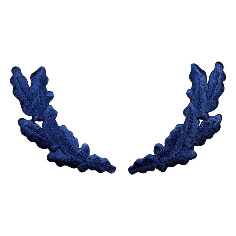 Pu&ograve; includere: Un paio di decorazioni in tessuto di foglie di quercia blu. Le foglie sono disposte in un motivo simmetrico, creando una forma di ghirlanda decorativa.