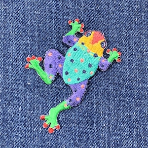 May include: A colourful embroidered frog patch with green, purple, blue, yellow, and orange accents. The frog has a spotted pattern and is perfect for adding a whimsical touch to clothing, bags, or other accessories.