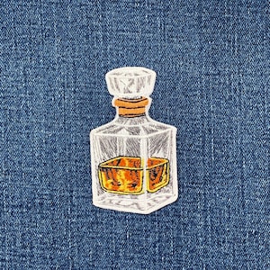 May include: An embroidered patch featuring a square glass decanter with a stopper. The decanter is outlined in white thread and filled with a golden-orange liquid. The stopper is a light tan color, and the entire design is set against a blue denim fabric.