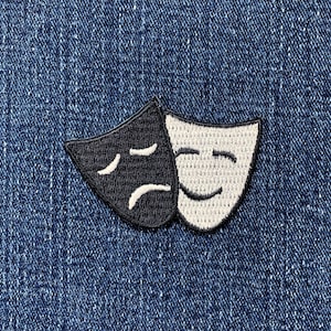 May include: Embroidered patch featuring the classic comedy and tragedy theater masks. The black mask depicts sadness, while the white mask shows happiness. The patch is stitched with white thread on a dark blue denim background.