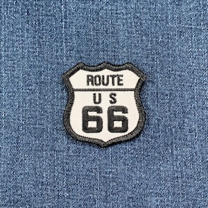 May include: A white and black Route 66 patch with a shield shape. The patch has black stitching around the edges.