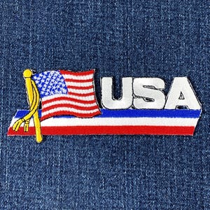Könnte beinhalten: Gestickter Aufnäher mit der amerikanischen Flagge und dem Wort "USA" in silbernen Buchstaben. Die Flagge hat rote und weiße Streifen und ein blaues Feld mit weißen Sternen. Der Aufnäher befindet sich auf einem blauen Jeanshintergrund.
