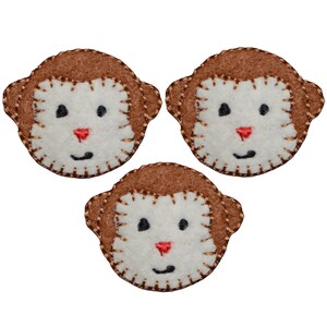May include: Three brown felt monkey faces with white faces and red noses. The monkey faces are stitched with a brown thread around the edges.