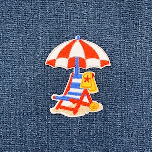 May include: Embroidered patch depicting a beach scene. A red and white striped parasol shades a blue and white striped deckchair. A yellow towel with a star and a seashell complete the design.