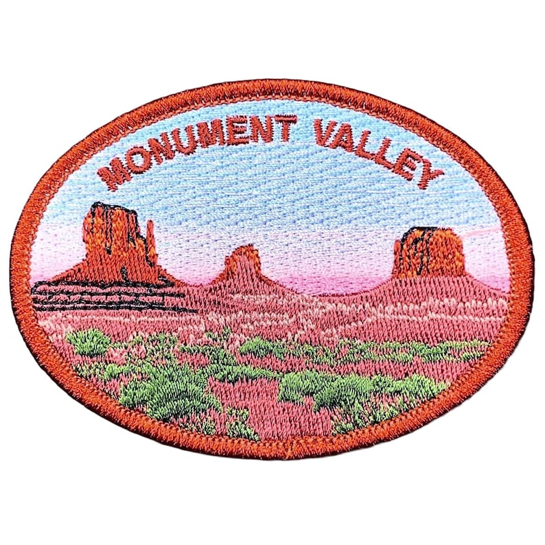 May include: Embroidered patch featuring a Monument Valley landscape with red rock formations, green shrubbery, and a blue and pink sky. The patch is oval-shaped with the words "MONUMENT VALLEY" in red lettering.