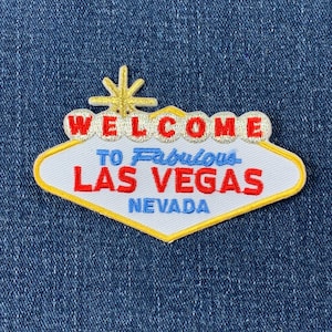 May include: A white and yellow embroidered patch with the text "Welcome to Fabulous Las Vegas Nevada". The patch is shaped like the iconic Las Vegas sign.