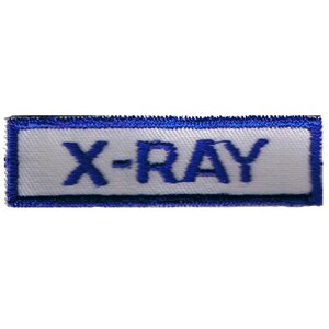 May include: A rectangular embroidered patch featuring a white background with a thick blue border. The text X-RAY is stitched in bold blue capital letters across the center of the patch, creating a clear and legible design for garment application.