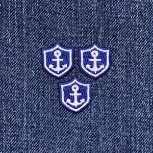 May include: Three navy blue and white anchor patches arranged on a blue denim background. Each patch is shield-shaped with a white anchor design. The patches are embroidered with a white border.