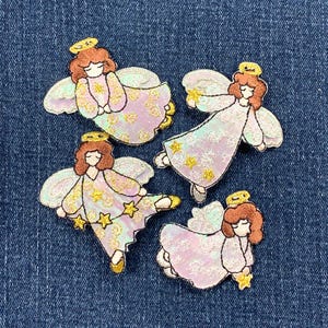 May include: Four embroidered angel patches with brown hair, gold halos, and wings. The angels wear pink and white dresses with gold star accents. The patches are on a blue denim background.