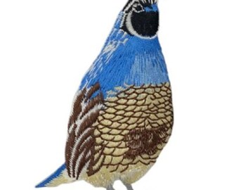 May include: Embroidered patch of a quail bird. The bird features a blue head and chest, with brown and tan patterned feathers on its body. The patch has a black head crest and gray feet, set against a white background.