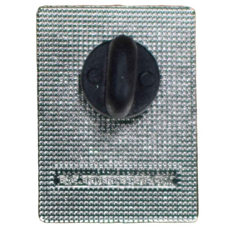 May include: The reverse side of a rectangular pin with a textured, silver surface. A black, rounded post is attached for securing the pin. The pin's surface has the text "BA RIVERSED" printed on it.