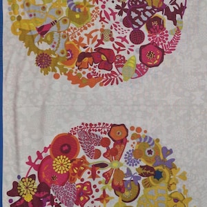 Op de afbeelding: Witte stof met twee grote, cirkelvormige bloempatronen. De ontwerpen zijn gevuld met bloemen, bladeren en botanische elementen in rood, geel, paars en blauw. De achtergrond is een licht, patroonwit, met een blauwe rand.