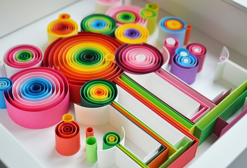 May include: A colorful paper quilling art piece featuring concentric circles and rolled paper shapes in a variety of vibrant colors, including red, orange, yellow, green, blue, and pink. The artwork is arranged in a white tray.