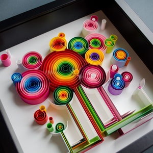 May include: A framed paper quilling art piece featuring colorful, concentric circles and linear elements. The artwork showcases a vibrant spectrum of colors, including red, orange, yellow, green, blue, and pink, arranged in a visually appealing composition.