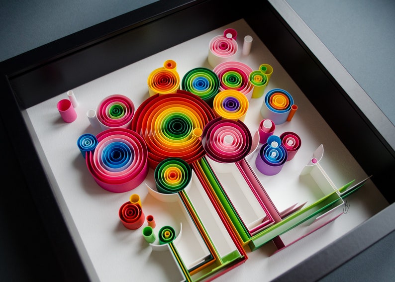 May include: A framed paper quilling art piece featuring colorful, concentric circles and linear elements. The artwork showcases a vibrant spectrum of colors, including red, orange, yellow, green, blue, and pink, arranged in a visually appealing composition.