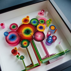 May include: A framed paper quilling art piece featuring a colorful abstract design. The artwork showcases concentric circles in a rainbow of colors, along with other rolled paper shapes, all set against a white background.