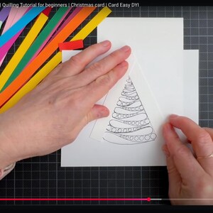 May include: A white card featuring a black line drawing of a Christmas tree with swirling patterns, surrounded by colorful paper strips in shades of pink, blue, green, orange, and yellow, along with crafting tools including tweezers and a white glue stick.