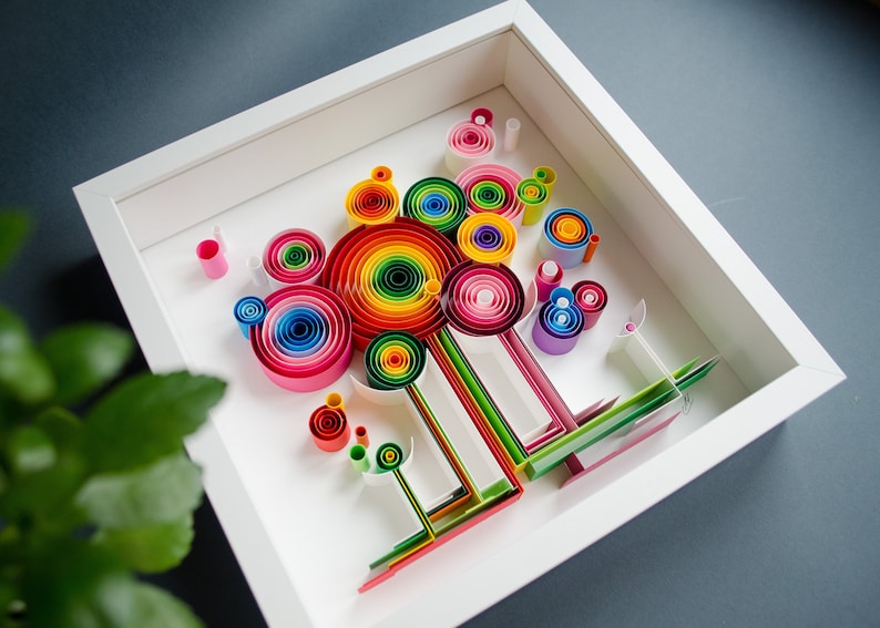 May include: A framed paper quilling art piece. The artwork features colorful, rolled paper designs in a variety of shapes and sizes, including spirals and lollipop-like structures. The color palette includes a rainbow of hues.