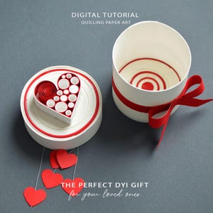 Könnte beinhalten: Digitales Tutorial für Papierquilling-Kunst. Das Bild zeigt einen weißen zylindrischen Behälter mit rotem Band und eine runde Box mit herzförmigem Design. Das Herz ist mit roten Papierrollen und weißen Kreisen gefüllt. Rote Papierherzen hängen darunter.