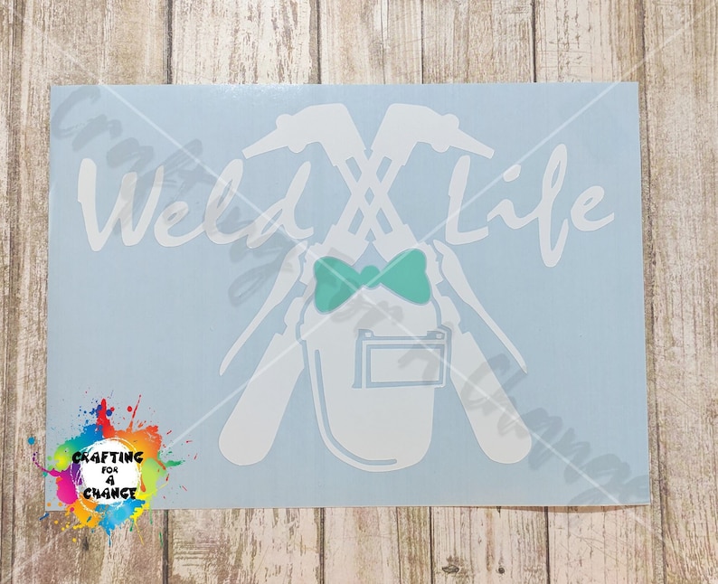 May include: A white decal on a light blue background with the words "Weld Life" in a script font. The design includes crossed welding tools, a welding helmet, and a teal bow tie. The decal also features a colorful logo that says "Crafting for a Chance."