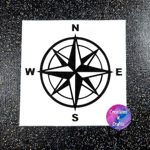 May include: Black compass rose design on a white square. The compass points to North, South, East, and West. The image is set against a black glitter background. A small, round logo in the bottom right corner reads "Creations N Crafts."