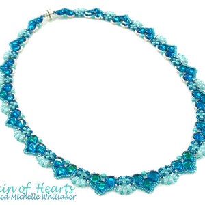 May include: A blue and turquoise beaded necklace with a silver clasp. The necklace is made of small, heart-shaped beads and is arranged in a pattern of alternating colors. The necklace is called "Chain of Hearts" and is designed by Michelle Whittaker.