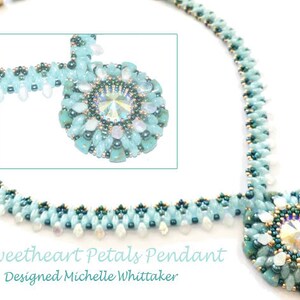 Op de afbeelding: Een lichtblauwe kralenketting met een bloemvormige hanger. De hanger heeft een centraal kristal en is omgeven door lichtblauwe en witte kralen. De ketting is gemaakt van kleine, lichtblauwe kralen. Tekst op de afbeelding luidt "Sweetheart Petals Pendant" en "Designed Michelle Whittaker."