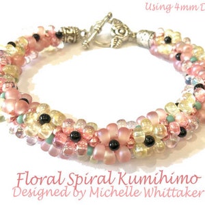May include: A floral spiral Kumihimo bracelet with pink, yellow, and black beads. The bracelet is designed with a flower pattern and has a silver clasp. The text "Using 4mm Drops" and "Designed by Michelle Whittaker" is visible.